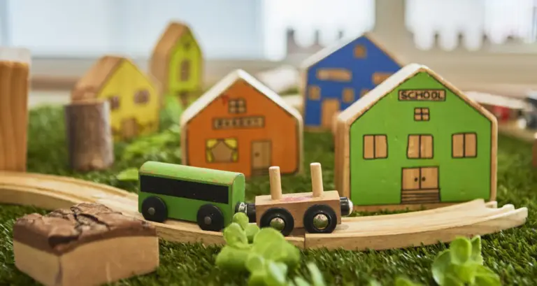 Wooden toy houses, a vehicle and small-world play materials.