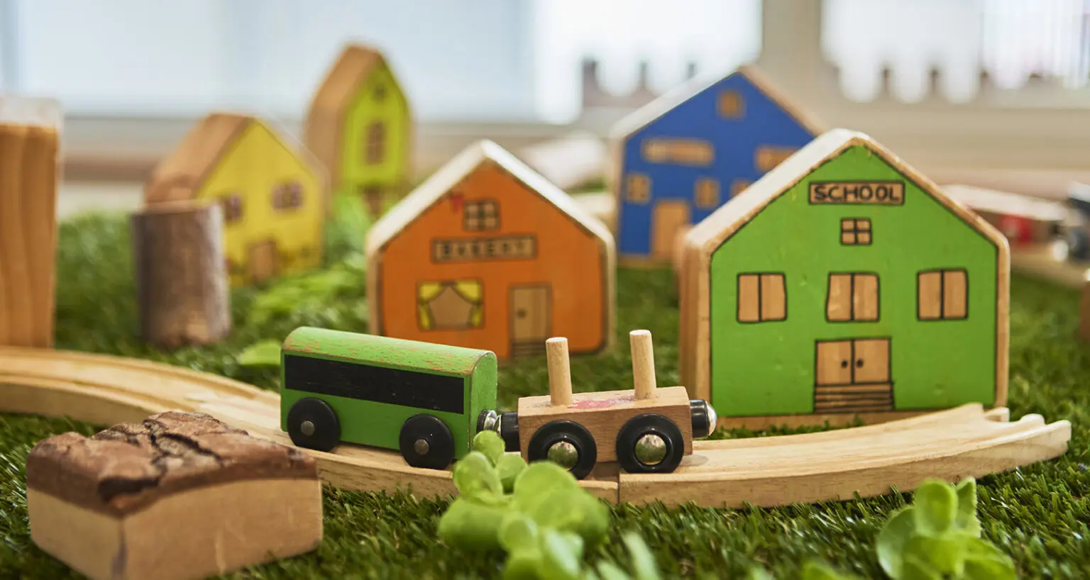 Wooden toy houses, a vehicle and small-world play materials.