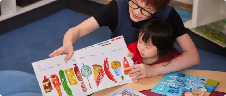 An educator and child sharing a colourful picture book.