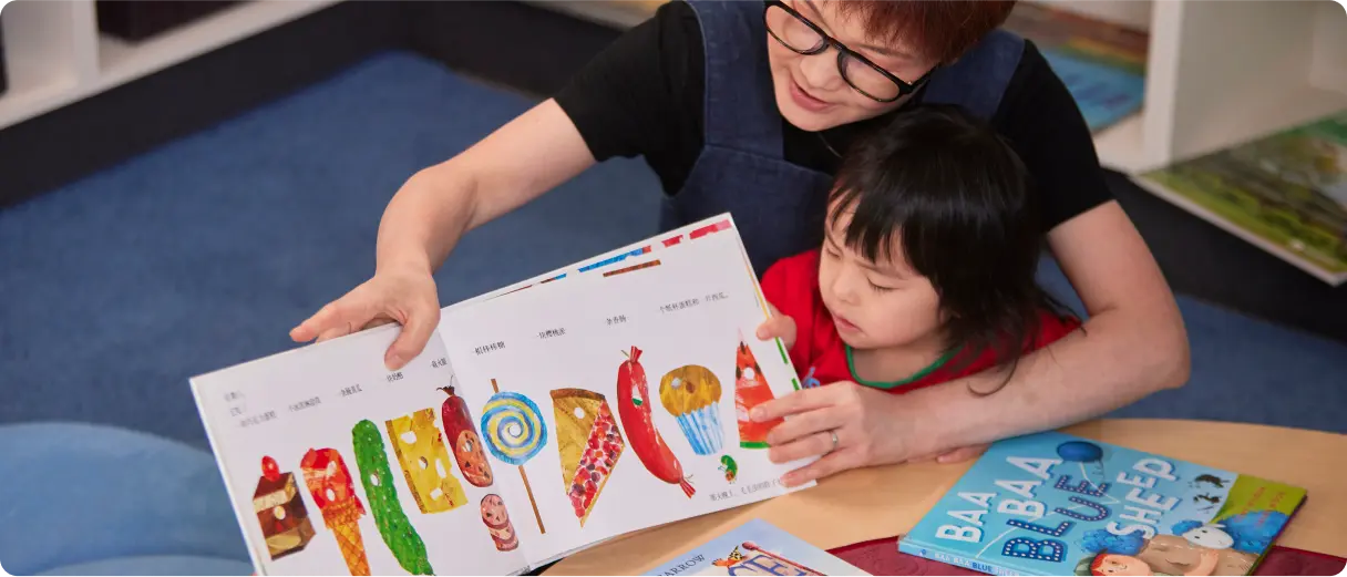 An educator and child sharing a colourful picture book.